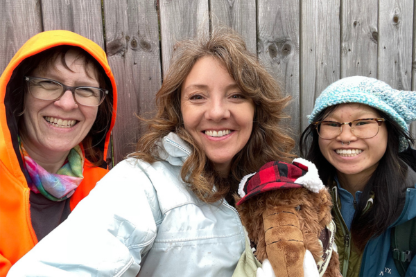 Three women take a selfie with a stuffed wooly mammoth.