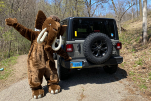 Monty the Mammoth poses in front of a Jeep Wranger sporting a sample of the Ice Age Trail Alliance license plate.