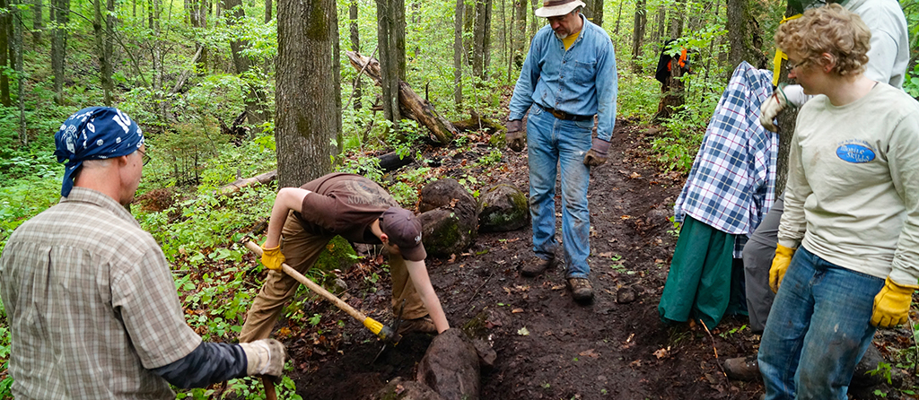Crew members look on as a volunteer places a rock while building new trail.