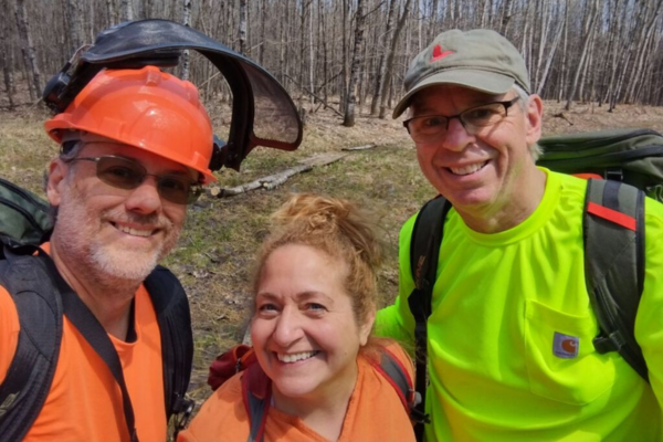 Three smiling volunteers wearing blaze orange and yellow take a selfie.