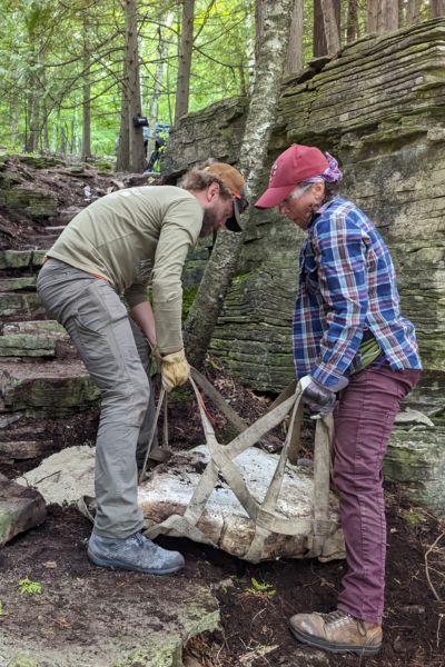Two volunteers work together to move a large rock.