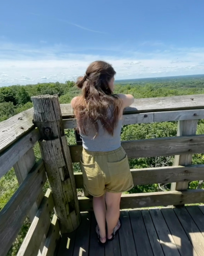 A woman stands at the top of an observation tower and enjoys the scenic forest views.