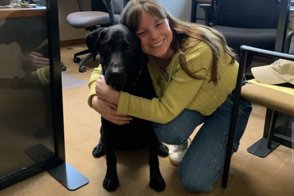 A young woman hugs a black lab.