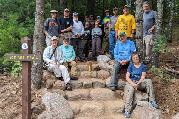 A group of volunteers sit and stand by a brand new stone staircase on the Ice Age Trail.