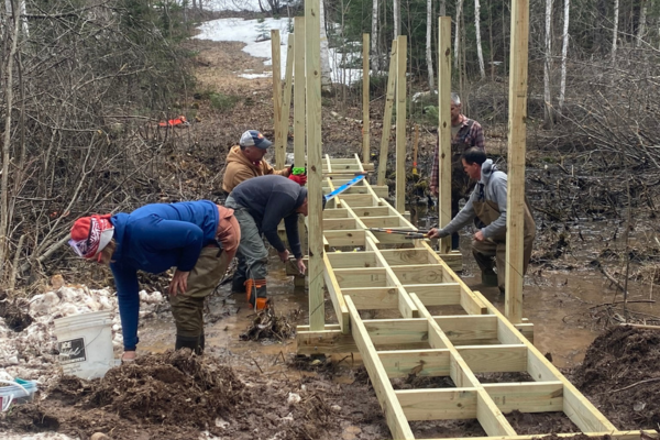 Volunteers work in the mud to construct a boardwalk frame.