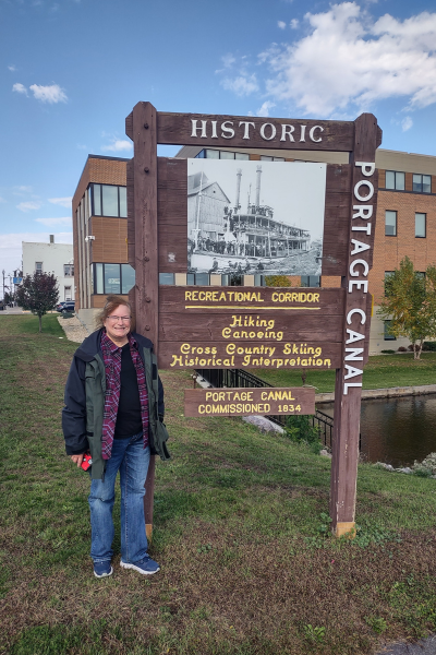 A woman poses next to the Portage Canal recreational corridor wooden sign.