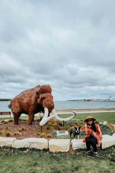 A woman and dog sit and pose next to a mammoth statue.