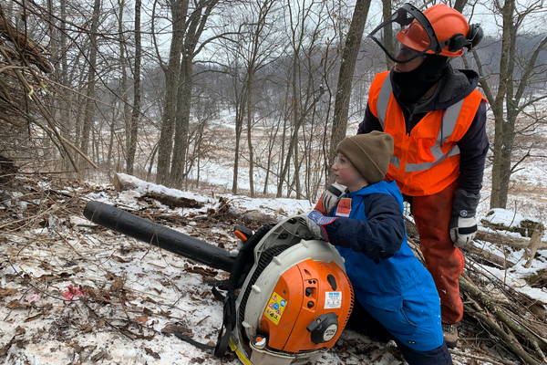 A sawyer helping a youth volunteer use the leaf blower to assist the brush fire.