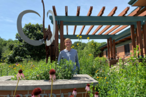 A man stands in front of a metal mammoth statue and among wildflowers.